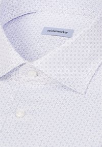 Chemise blanche avec petit motif géométrique bleu, col plié, boutons blancs et étiquette "seidensticker" à l'intérieur du col.