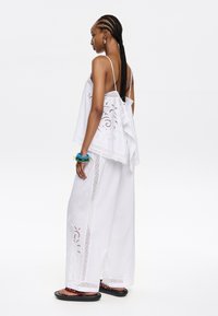 Witte mouwloze top met geborduurde details en een losse pasvorm, gecombineerd met brede witte broek met kantaccenten en een vloeiende stijl.