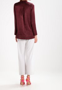 Burgundy satin skjorta med lång ärm och en ryggveck, ihop med vita vida byxor och rosa högklackade sandaler.