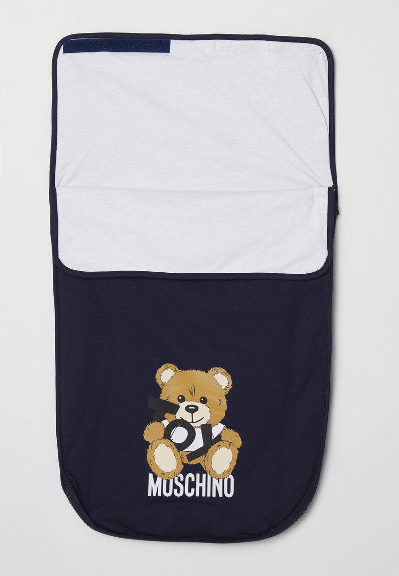 Jūras spēku guļammaiss ar baltu augšdaļu. Apskatāma multiplikācijas varoņa lācīša attēls, kurš tur futbolu, un zem tā ir uzraksts "MUSCHINO". Gluda tekstūra.