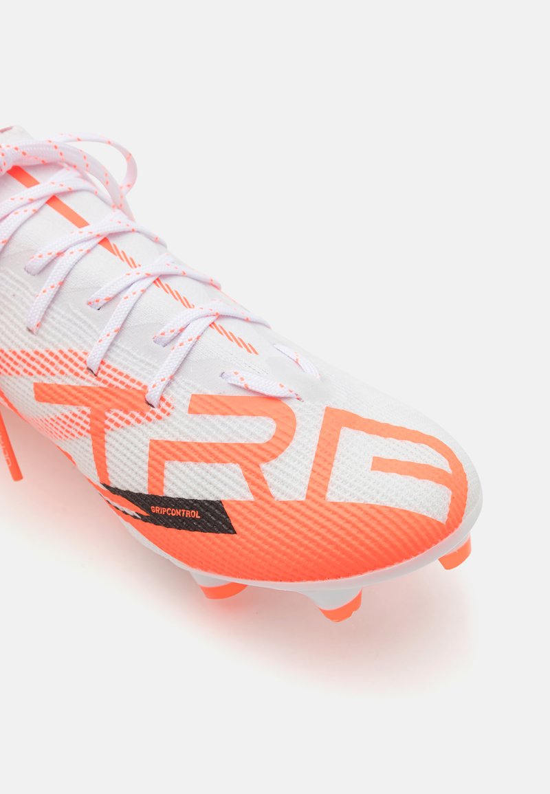 Crampons de football blanches avec des accents orange néon, matériau texturé et grand logo "TRB". Présente un détail "GRIPCONTROL" noir et un laçage blanc.