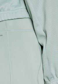 Jasnozielony sportowy komplet na górę i dół wykonany z teksturowanego, oddychającego materiału z gładkimi akcentami. Na szwach widoczne są detale szwów.