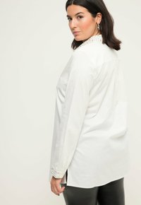 Hvid langærmet skjorte med en skræddersyet krave, lige pasform og sideskår. Stof er glat med en let glans.