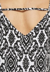 Tessuto a motivi bianco e nero con un design intricato e simmetrico, dotato di scollatura a V e dettaglio con bretelle incrociate.