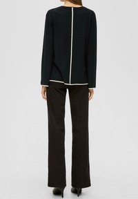 Zwarte lange mouw top met een contrasterende witte naad in het midden en bij de manchetten, gecombineerd met zwarte rechte broek en hakken.