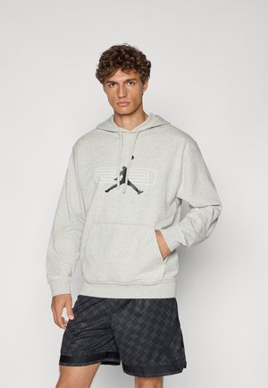 Lys grå hoodie med kængurulomme, snørelukke i hætten og sort logo print, parret med mønstrede sorte shorts. Blødt stof tekstur.