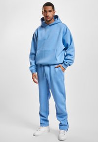 Helle blaue Kapuzenjacke mit Kängurutasche, kombiniert mit passenden, schmal zulaufenden Sweatpants. Aus weichem Stoff gefertigt, mit einem dezenten Logo-Detail.