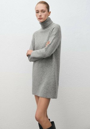 Vestido de suéter gris de punto con cuello alto, mangas largas, textura suave y corte relajado, llegando a la mitad del muslo, combinado con botas negras hasta la rodilla.