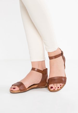 Sandales en cuir marron avec un dos fermé, de larges bretelles sur les orteils et une bride à la cheville. Texture douce et semelle plate.