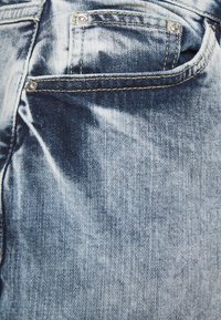 Light blue denim jeans with a faded wash, featuring a back pocket, silver hardware, and stitching detail. Soft texture with a classic design.