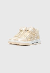 Crème-kleurige hoge sneakers voor kinderen met klittenbandsluitingen, decoratieve studs aan de zijkanten en de tekst "Crazy Beautiful" op de witte zolen.