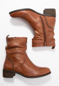 Ein Paar mittelhohe braune Lederstiefel mit seitlichen Reißverschlüssen, niedrigem Blockabsatz und einem leicht schlappen Design auf weißem Hintergrund.