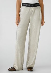 Metalen zilveren wijde broek met een gestructureerde afwerking en een zwarte elastische tailleband met een herhaald logo patroon.