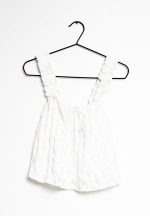 Witte katoenen top met gerimpelde schouderbanden, voorzien van een gestructureerd bloemenpatroon en een losse pasvorm. Hangt aan een zwarte metalen hanger.