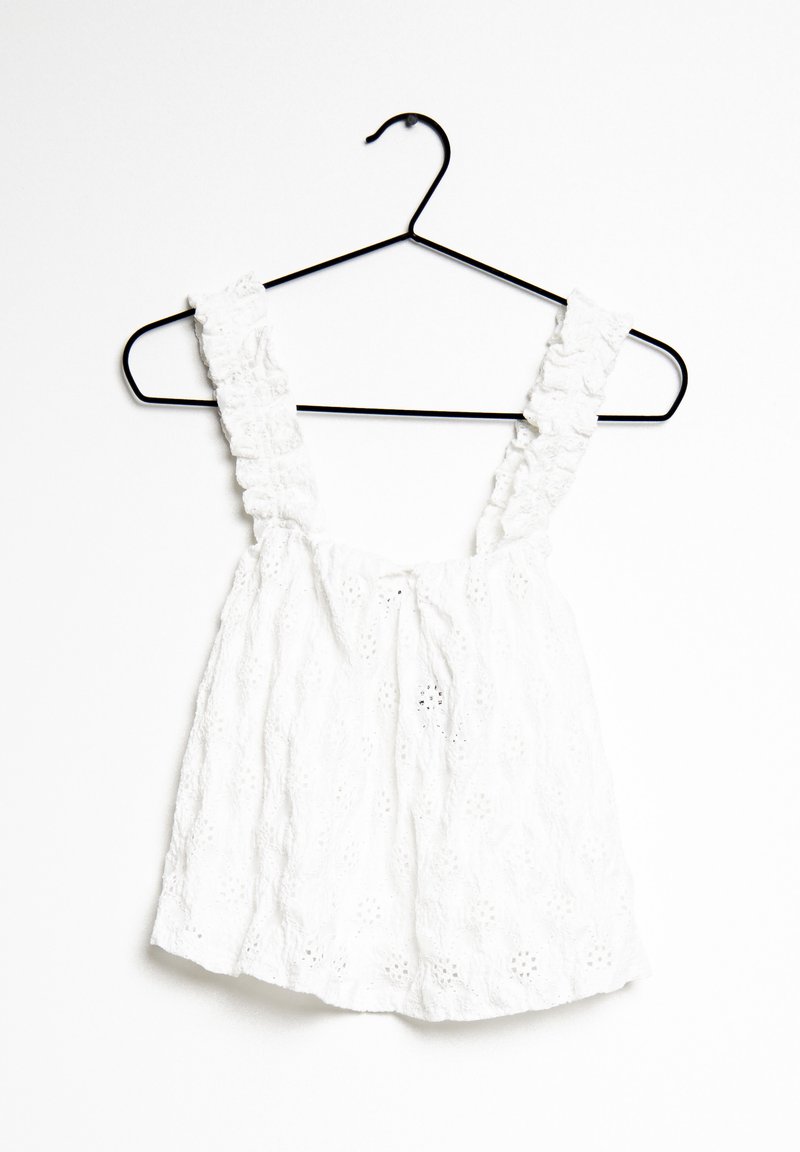 Witte katoenen top met gerimpelde schouderbanden, voorzien van een gestructureerd bloemenpatroon en een losse pasvorm. Hangt aan een zwarte metalen hanger.