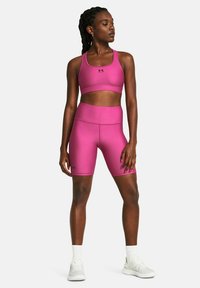 Conjunto deportivo rosa con un sujetador deportivo ajustado y pantalones cortos de cintura alta, fabricado en tejido suave. Presenta un logo de Under Armour en negro.