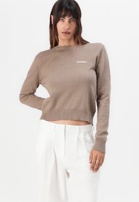 Brun ribbet strikkegenser med rund hals og cropped hem. Har "2ND DAY" logo i hvitt. Kombinert med skreddersydde hvite bukser.