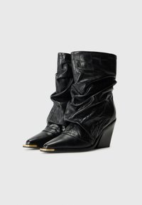 Black slouchy leather ankle boots with pointed toes, embossed texture, metallic toe caps, and stacked wedge heels.