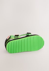 Zwarte en groene sandaal met een groen rubberen zool met textuur en verstelbare bandjes. De zool heeft verticale strepen voor extra grip.