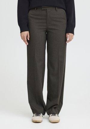 Pantalons ajustés marron foncé à coupe droite, présentant une texture subtile et un pli, associés à des baskets de couleur claire.