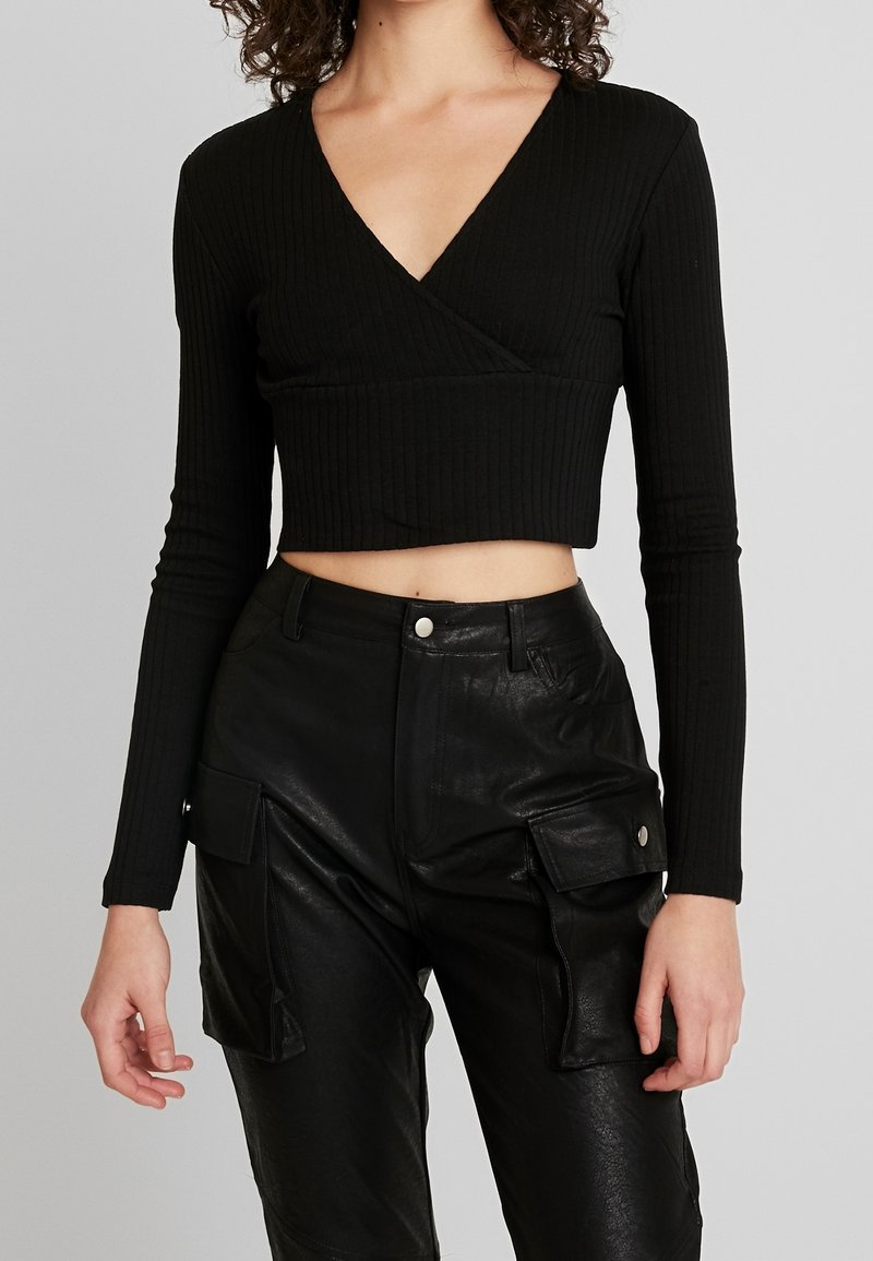 Schwarzes, geripptes langärmeliges Wickel-Crop-Top mit tiefem V-Ausschnitt, kombiniert mit hochtaillierten schwarzen Cargo-Hosen aus Kunstleder mit seitlichen Taschen.