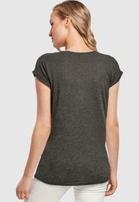 Mørkegrå t-shirt med rullede korte ærmer, blød tekstur, rund nederkant og subtil syning, båret med hvide bukser.