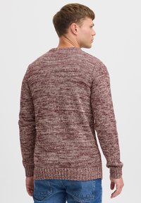 Pull en tricot bordeaux avec un motif texturé. Comprend des manches longues et un col et un ourlet côtelés. Porté sur un jean bleu.