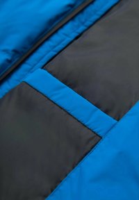 Sinisen ja mustan sävyinen eristetty takin kangas, jossa on sileä pinta; siinä on vastavärinen sininen raita ja suuri, tumma laskostasku.