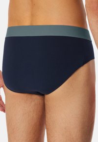 Marineblaue Unterwäsche mit einem weichen, grünen Bund. Verfügt über eine glatte Textur und ein enges Design mit minimaler Abdeckung von hinten.