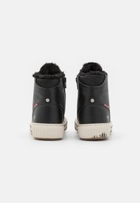 Bottines en cuir noir avec doublure en fausse fourrure, fermeture éclair, et une semelle en caoutchouc crème présentant des rayures verticales et un léger usure.
