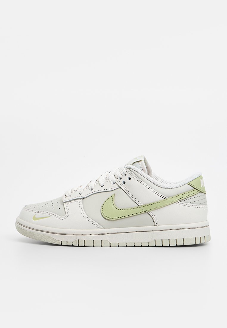 Baskets en cuir blanc avec des accents vert clair, boîte à orteils perforée et semelle en caoutchouc. Présente un logo prominent sur le côté et à l'arrière.