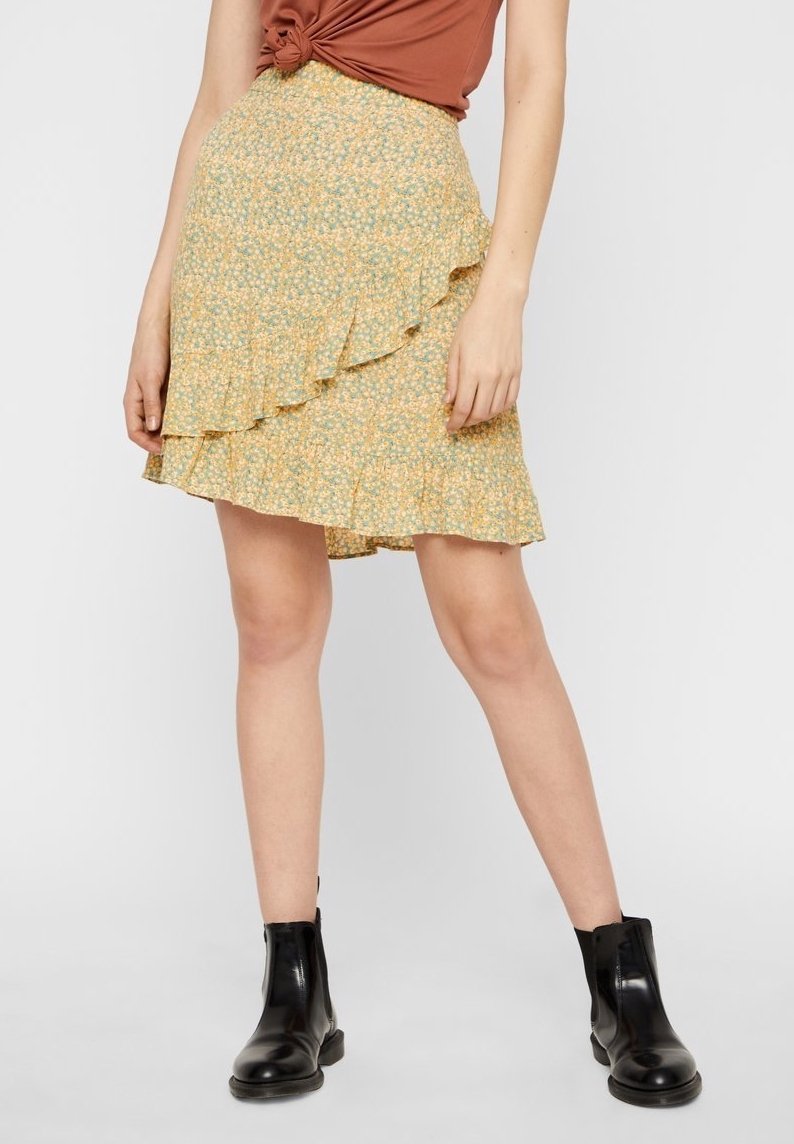 Světle žlutá květinová sukně s vrstvenými volány, vyrobená z měkkého materiálu. Nositá s hnědým topem a černými kotníkovými botami.