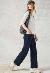 Hellgraue gerippte Strickjacke mit Knöpfen, kombiniert mit dunkelblauen weiten Jeans und weißen Sneakers. Eine graue Mütze rundet den Look ab.