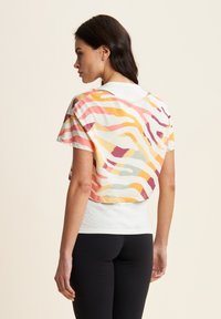 T-shirt cropped con una stampa astratta colorata con strisce ondulate arancioni, rosa e verdi su uno sfondo chiaro. Tessuto morbido.