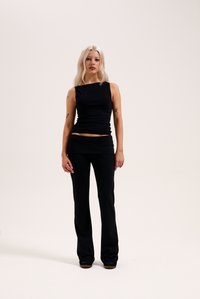 Juodas be rankovių viršus ir prigludusios, platėjančios kelnės iš lygios medžiagos. Šis drabužių rinkinys pasižymi minimalizmu, yra prigludęs ir vientisos spalvos.