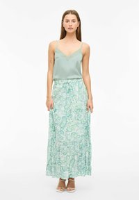 Camisón de satén verde menta con encaje, combinado con una falda maxi fluida y estampada en un diseño de paisley con tonos verdes y blancos.