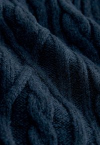 Dunkelblaues gestricktes Material mit einem strukturierten Kabelmuster. Der Stoff wirkt weich und flauschig, mit unterschiedlichen Dicken im gesamten Gewebe.