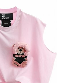 Top sin mangas de color rosa con un peluche de oso de felpa que lleva un conjunto negro y una capucha rosa, mostrando el texto "MWM" en el atuendo del oso.