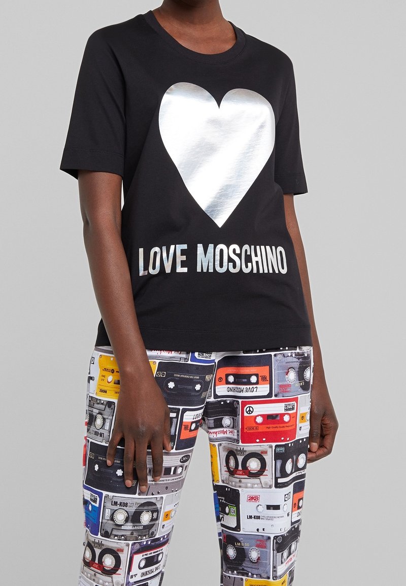 Black cotton t-shirt featuring a large silver heart graphic and "LOVE MOSCHINO" text in silver, paired with patterned multicolored cassette tape leggings.