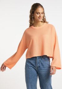Pull léger, court en corail doux avec texture côtelée et manches larges, associé à un jean en denim bleu taille haute.
