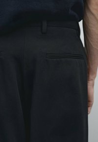 Black dress pants with a smooth texture, featuring a single back pocket with a narrow trim. Belt loop visible at the waist.