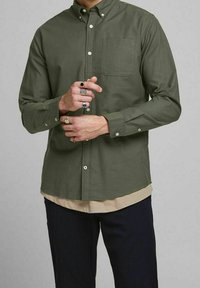 Camicia verde oliva con colletto, tasca singola sul petto e maniche lunghe. Presenta una texture liscia e bottoni bianchi.