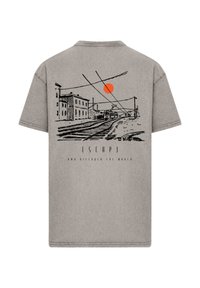 Gray cotton t-shirt featuring a black line drawing of a city scene with a red sun. Text below reads "ESCAPE AND DISCOVER THE WORLD."
