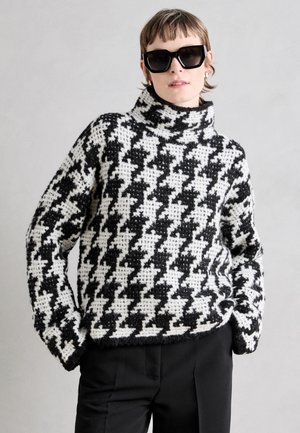 Black and white houndstooth-patterned turtleneck sweater with a soft, textured knit. Loose fit, long sleeves, and ribbed hem.