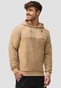 Sudadera con capucha beige que presenta un diseño de canalé texturizado, bolsillo frontal tipo canguro, cierre con cordón y puños ajustados.