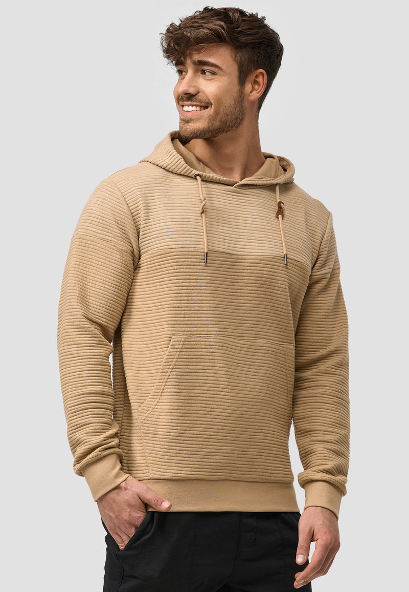 Sudadera con capucha beige que presenta un diseño de canalé texturizado, bolsillo frontal tipo canguro, cierre con cordón y puños ajustados.