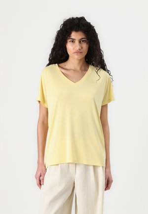 Yellow short-sleeve V-neck t-shirt made of smooth material, displayed with neutral-colored loose-fitting pants. Minimalist design, no patterns.