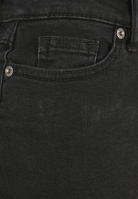 Nahaufnahme einer schwarzen Jeans-Tasche aus Denim mit sichtbaren Nähten und zwei Metallnieten an den oberen Ecken.