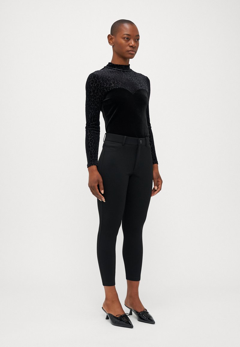 Top in velluto nero con motivo leopardato e collo alto; pantaloni neri aderenti; scarpe nere lucide a punta con dettagli in pizzo.