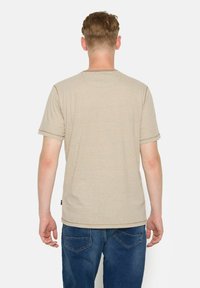 Camiseta de manga corta beige con finas rayas horizontales, escote redondo y un corte relajado, combinada con jeans azules y un dobladillo pronunciado.